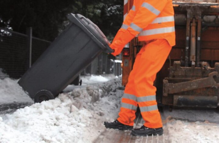 Müllwerker zieht Tonne über Schnee