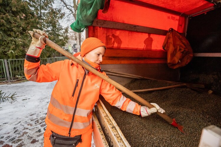 BSR-Beschäftigte lädt Splitt auf eine Schaufel