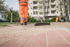 Reinigungskraft der BSR fegt Weg auf einem Spielplatz