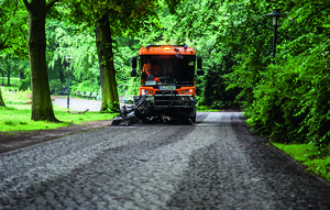 Mittelgroße Kehrmaschine reinigt Gehweg im Park.